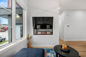 Una sala de estar moderna con chimenea, una ventana con vistas a la calle, un sofá azul y una mesita con velas.