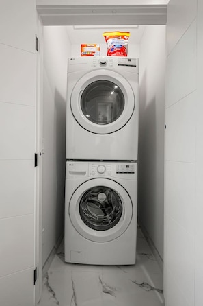 A laundry room with two stacked front-loading washing machines and detergent bottles on top. - ‘Indigo’ 3 Bedroom | Garage | King + 7 Min to DT (Calgary)