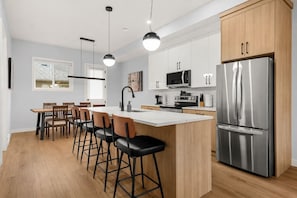 A modern kitchen with a central island, bar stools, stainless steel appliances, and pendant lighting. - ‘Indigo’ 3 Bedroom | Garage | King + 7 Min to DT (Calgary)