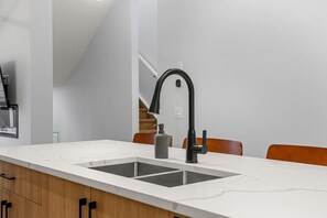 Una cocina moderna con encimera blanca, grifo negro y mueble de madera.