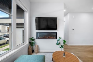 A modern living room with a fireplace, a flat-screen TV, and a view of the outside. - `The Juniper` 3 Bed | King | Garage | 5 Min to DT (Calgary)
