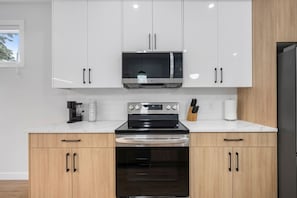 A modern kitchen with white cabinets, a stainless steel microwave, an oven, and a coffee maker. - `The Juniper` 3 Bed | King | Garage | 5 Min to DT (Calgary)