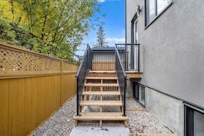 A wooden staircase leading to a balcony with a metal railing, surrounded by a wooden fence and trees. - `The Juniper` 3 Bed | King | Garage | 5 Min to DT (Calgary)