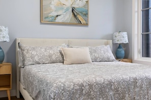 A bedroom with a bed, floral-patterned bedding, a painting above the bed, and two bedside lamps. - ‘Rowan’ 3 Bed | Garage | King + 7 Min to DT (Calgary)