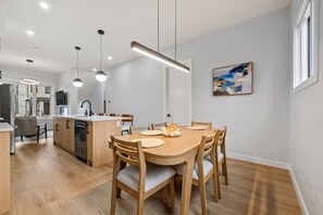 A modern kitchen with wooden cabinets, a dining table with chairs, and pendant lighting. - ‘Rowan’ 3 Bed | Garage | King + 7 Min to DT (Calgary)