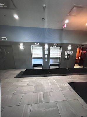 An elevator area with two elevators, a tiled floor, and a wall-mounted sign. - `Skyline` Downtown Core | AC | Walk to Saddledome (Calgary)