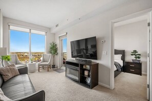 A modern living room with a flat-screen TV, a sofa, a chair, and a small table. There is a balcony with a view of the city. - `Skyline` Downtown Core | AC | Walk to Saddledome (Calgary)