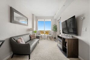 A modern living room with a grey sofa, a flat-screen TV, and a balcony with a city view. - `Skyline` Downtown Core | AC | Walk to Saddledome (Calgary)