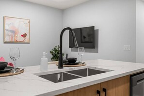 A modern kitchen with a black faucet, two sinks, a marble countertop, and a potted plant. - `Paris` King Bed | 7 Mins to DT + Free Parking (Calgary)