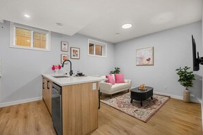 Una cocina moderna con una isla central, una zona de comedor con un sofá y una mesa de centro, y un espacio de sala de estar con un diván y una alfombra.