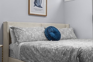 Una cama con ropa de cama estampada con motivos florales y una única almohada decorativa azul.