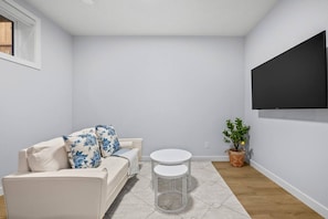 A room with a white sofa, a small round table, a potted plant, and a mounted TV. - `Greece` King Bed | Private Suite + 7 Min to DT (Calgary)