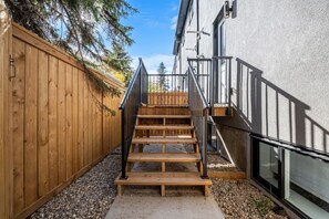Gradi de fusta que condueix a un edifici, amb barana metàl·lica, envoltat per una tanca de fusta i un sòl de grava.