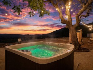 Ein Whirlpool mit Blick auf einen Sonnenuntergang und einen Baum mit Lichterketten.