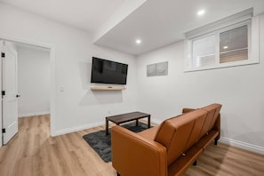 A modern living room with a sofa, a coffee table, and a flat-screen TV mounted on the wall. - The Nook | 2 Bedroom | Close to DT Hospital & UofC (Calgary)