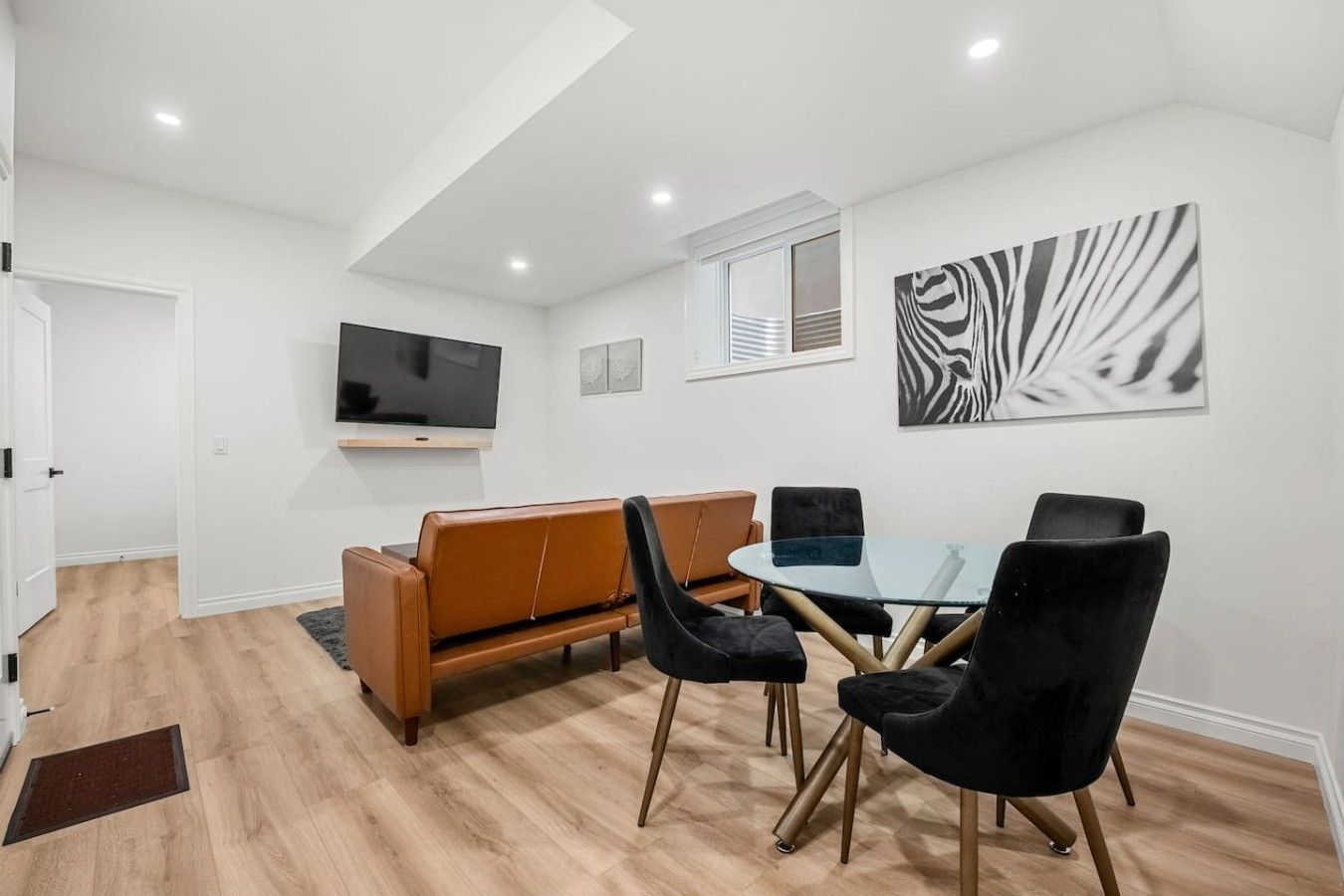 Ein modernes Wohnzimmer mit einer Couch, Sesseln, einem Glastisch, einem Flachbildfernseher und Kunstwerken an der Wand.