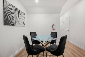 Una habitació amb una taula rodona de vidre envoltada per quatre cadires negres, una obra d'art amb estampat de zebra a la paret, i un extintor fixat a la paret.