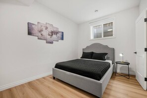 A bedroom with a bed, a nightstand, a window, and wall art. - The Nook | 2 Bedroom | Close to DT Hospital & UofC (Calgary)