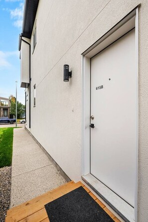 A modern building exterior with a white door marked '615B' and a small black outdoor light fixture. - The Nook | 2 Bedroom | Close to DT Hospital & UofC (Calgary)