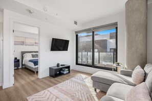 Ein modernes Schlafzimmer mit einem Bett, einem Fernseher, einem Nachttisch und einem großen Fenster.