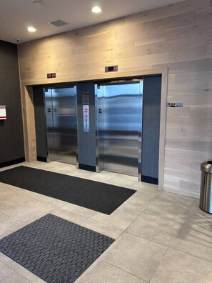 An elevator area with two elevators, a black mat, and a trash can. - The Ivory | 2 Bedroom | UG Parking | Rooftop Patio (Calgary)