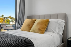 A bed with a grey headboard, two pillows, and a striped blanket. - The Ivory | 2 Bedroom | UG Parking | Rooftop Patio (Calgary)