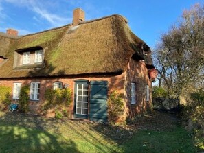 Ein traditionelles Reetdachhaus mit Backsteinfassade, einer grünen Tür und einem kleinen Garten.
