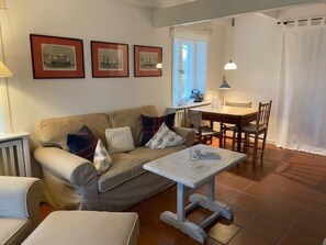 Olohuoneessa on sohva, sohvapöytä, ruokapöytä tuoleineen sekä seinällä olevia kehystettyjä tauluja.