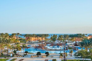 A resort with multiple swimming pools, palm trees, and beach umbrellas. - Luxurious new cairo hotel apartments (New Cairo City)