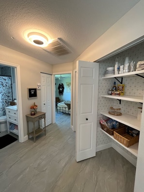 Ein gut beleuchteter Flur mit einer weißen Tür zu einem Schlafzimmer, einem kleinen Tisch mit einer Vase und einem Regal mit diversen Gegenständen.