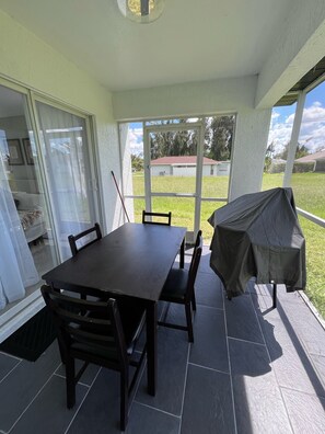 An outdoor patio with a table and chairs, a covered grill, and a view of a grassy area. - Cozy 3-bedroom home near Warm Mineral Springs, mayakka river, and gulf beaches (North Port)