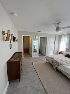 Ein Schlafzimmer mit einem Bett, einer Kommode, einem Deckenventilator und Blick auf ein Badezimmer.