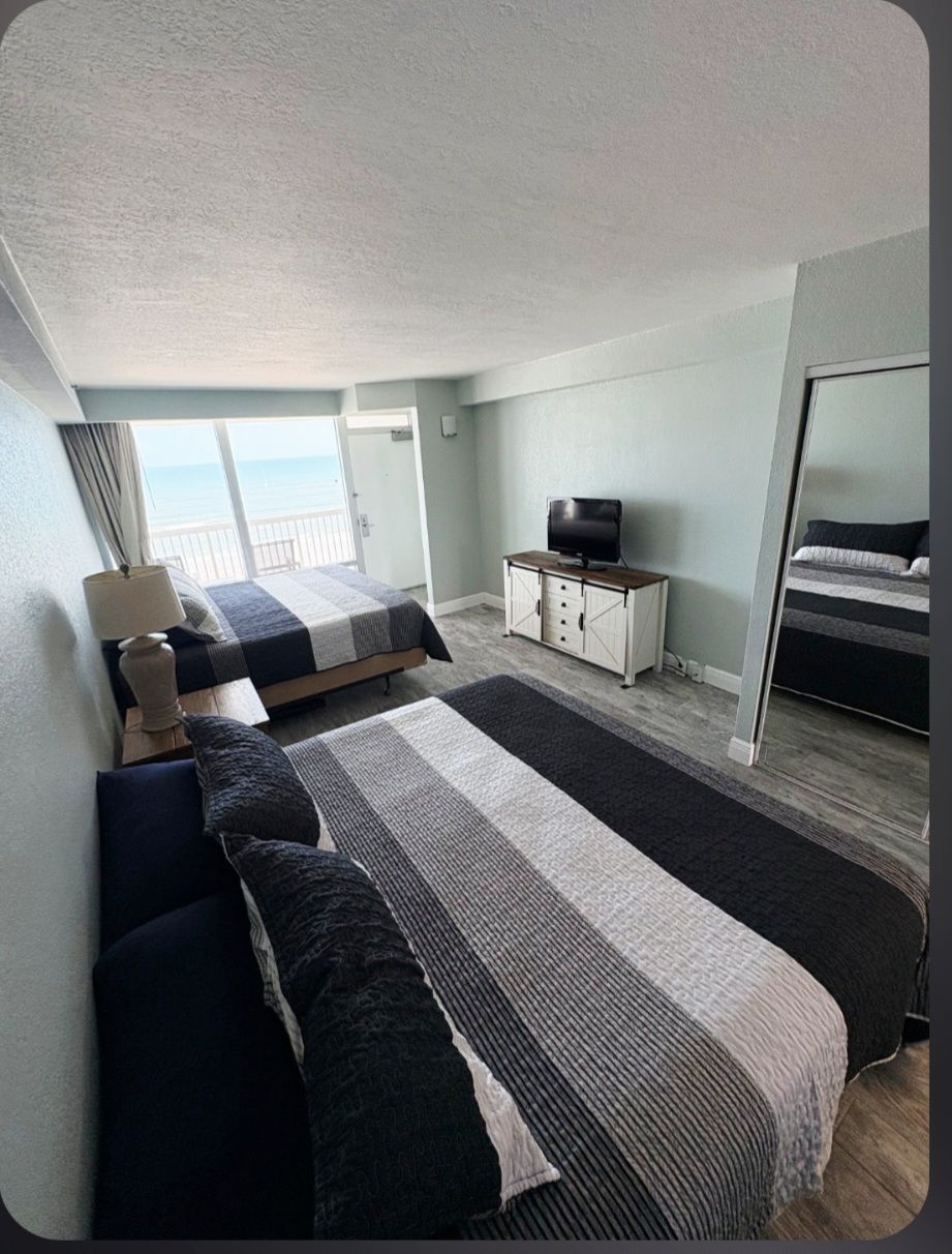 Une chambre avec deux lits, un téléviseur posé sur une commode et une vue sur la mer.