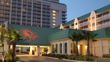 A hotel with a green roof, multiple balconies, and a palm tree-lined entrance.