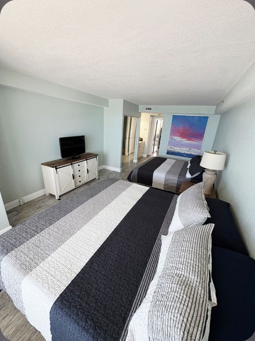 Spacious coastal bedroom with two queen beds, TV, and calming decor.