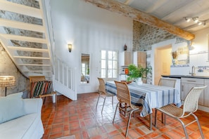 A spacious dining area with a high table and wicker chairs, a staircase with white railings, and a kitchen with stone walls and wooden beams. - Holiday Home 'Mas Bousquette' with Private Pool, Private Terrace and Wi-Fi (Lussan)