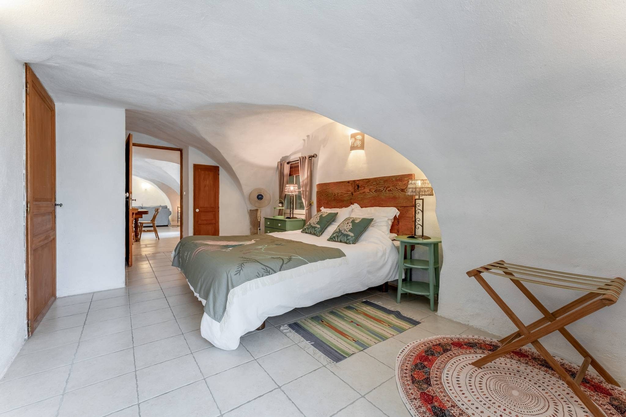 A bedroom with a bed, a nightstand, a lamp, a chair, and a view of a dining area.