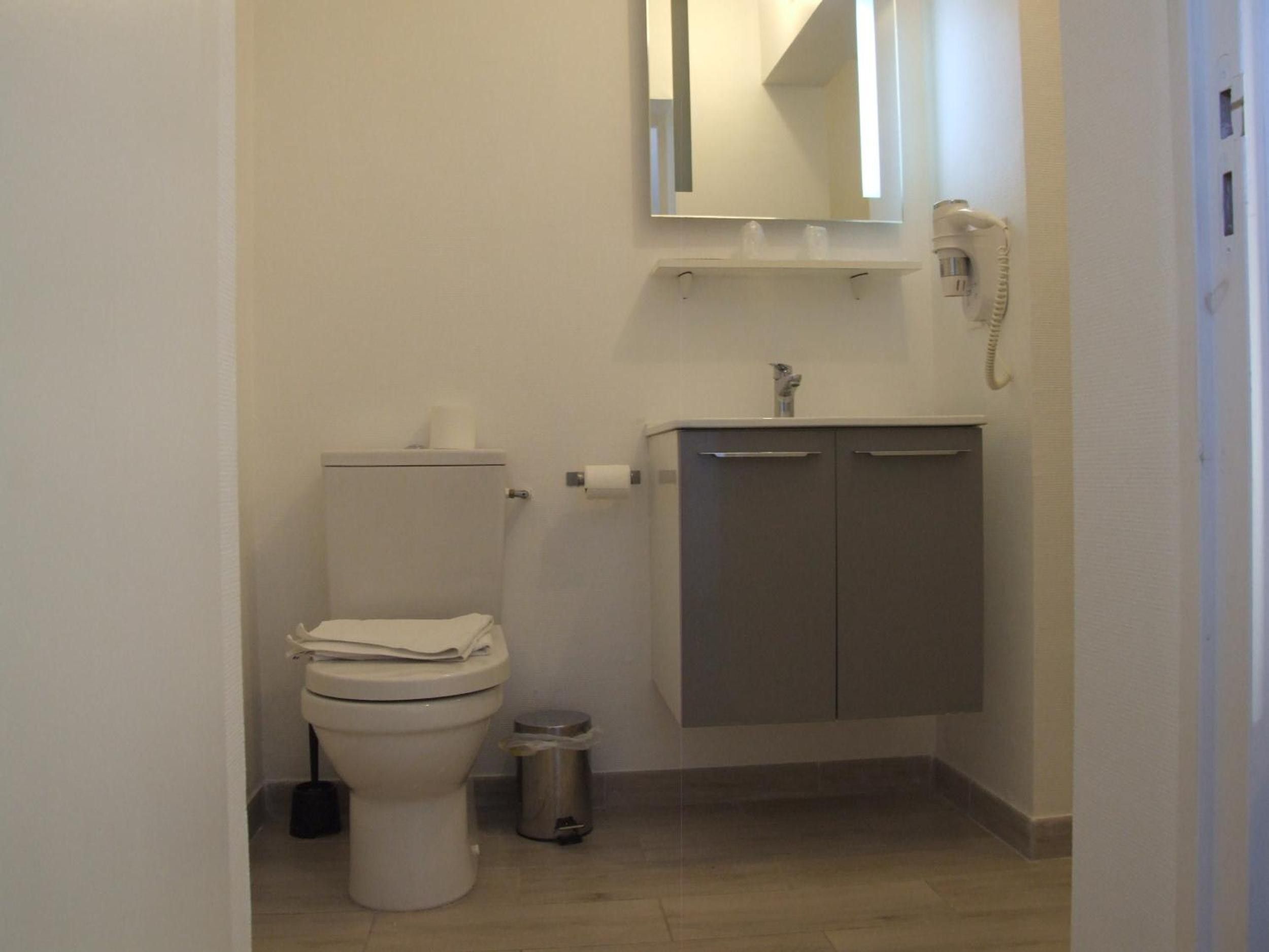 Een kleine, compacte badkamer met toilet, wastafel, spiegel en prullenbak.