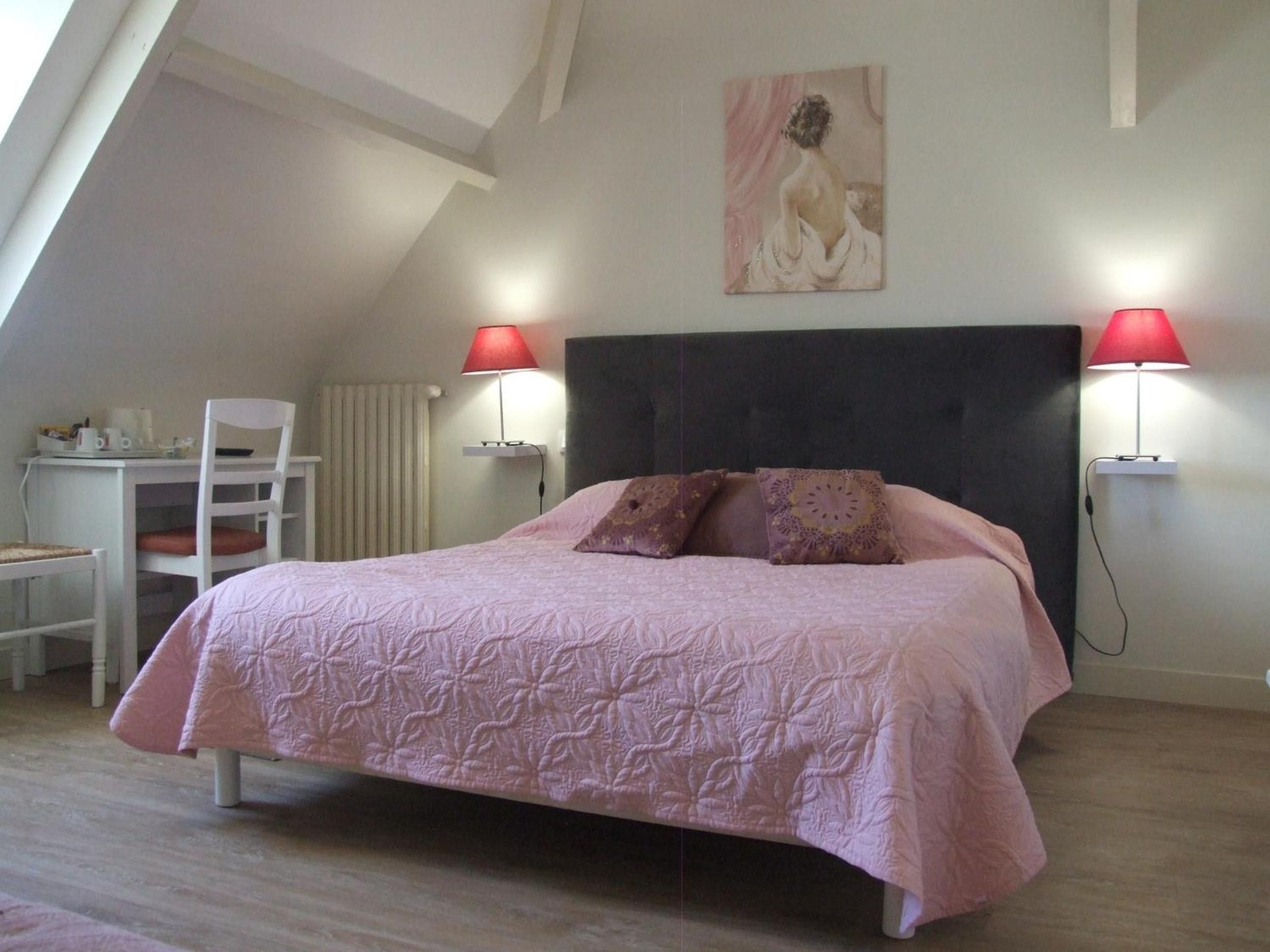 A bedroom with a bed, two bedside lamps, a chair, a desk, and a painting on the wall.