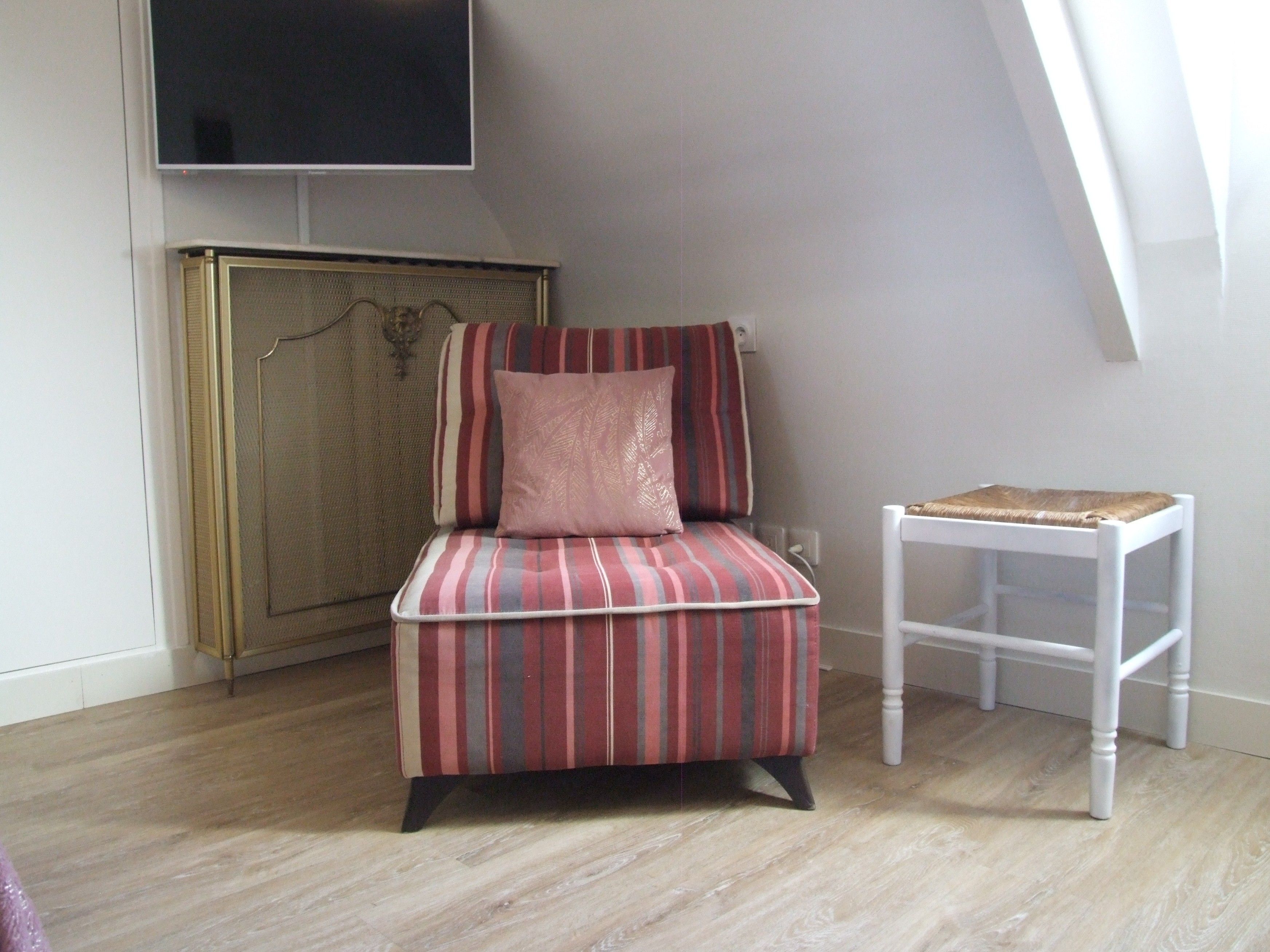 Una habitación de esquina con un sillón a rayas, una mesita blanca y un televisor montado en la pared.