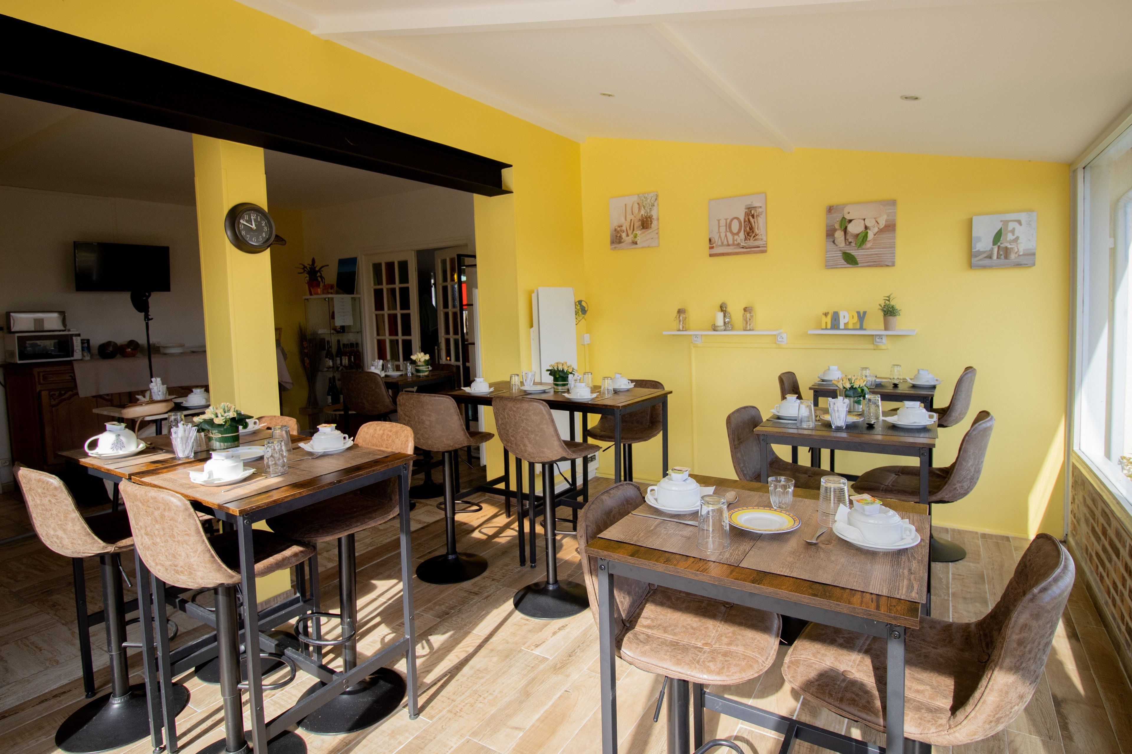 Un comedor con varias mesas y sillas, un reloj en la pared y una cocina al fondo.