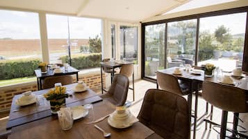 A dining area with tables set for two, featuring a view of a field through large windows.