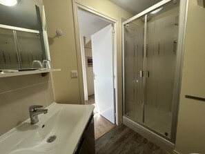 Un baño con lavamanos blanco, espejo y cabina de ducha de vidrio.