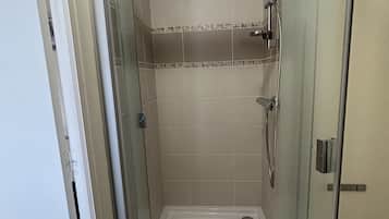 A glass-enclosed shower stall with a white floor, a handheld showerhead, and a wall-mounted faucet.