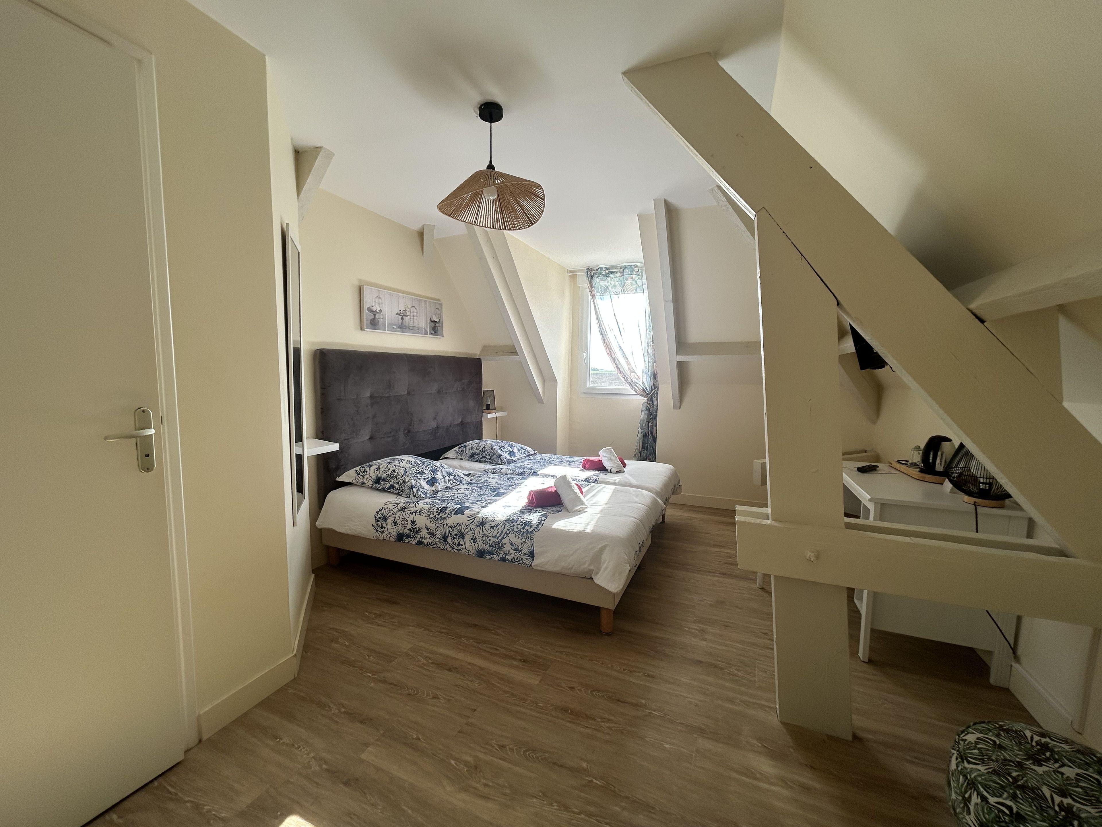 Un dormitorio con una cama, una lámpara colgante, una ventana con cortinas y una escalera.