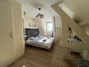 Un dormitorio con una cama, una lámpara colgante, una ventana con cortinas y una escalera.