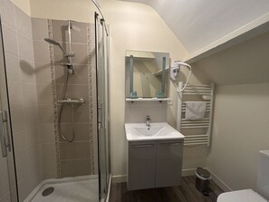 Un baño con ducha envuelta en vidrio, un lavabo con espejo y un perchero para toallas.