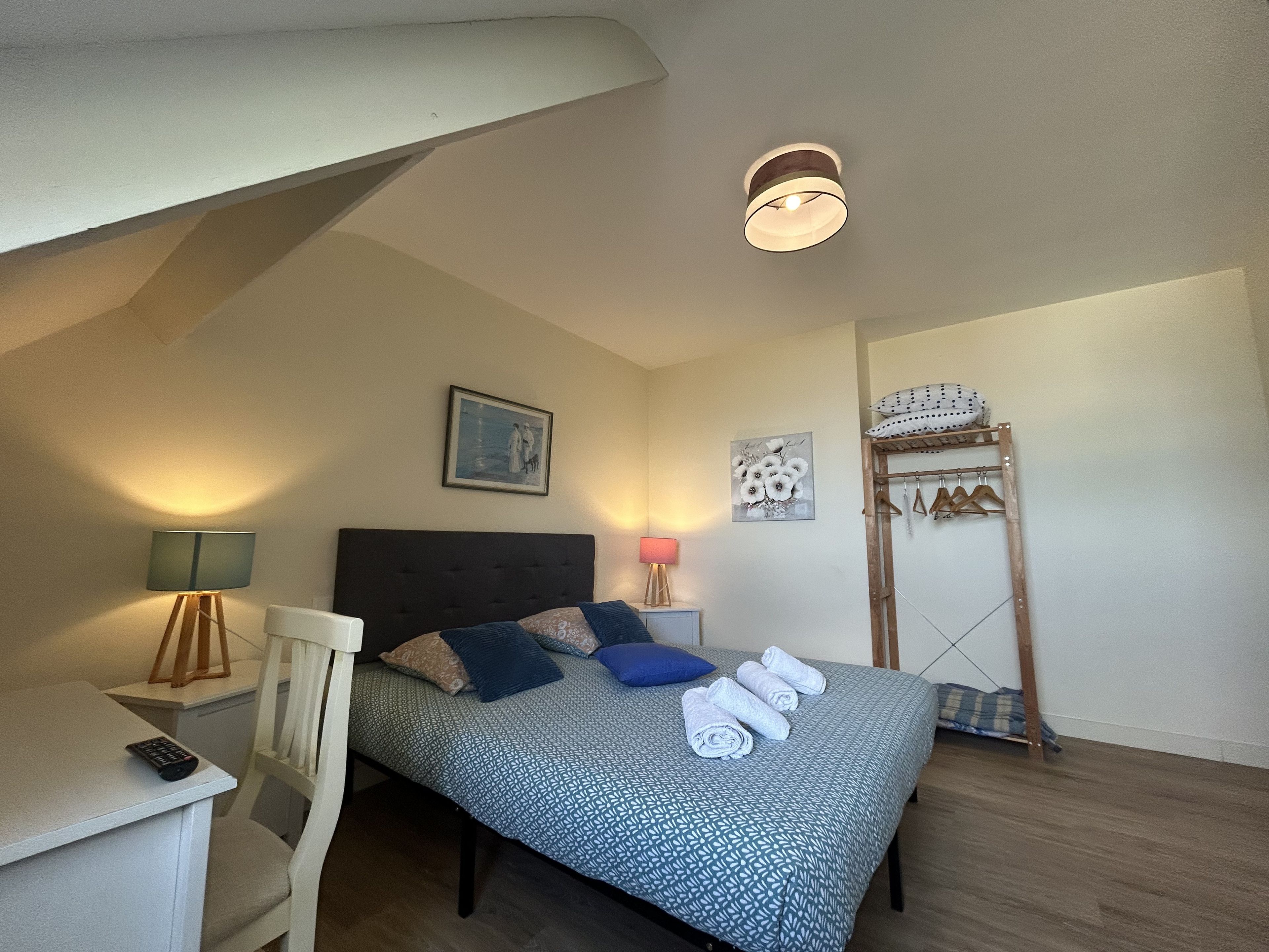 Une chambre à coucher comprenant un lit, un bureau, une chaise, une lampe, un tableau accroché au mur et une échelle en bois.