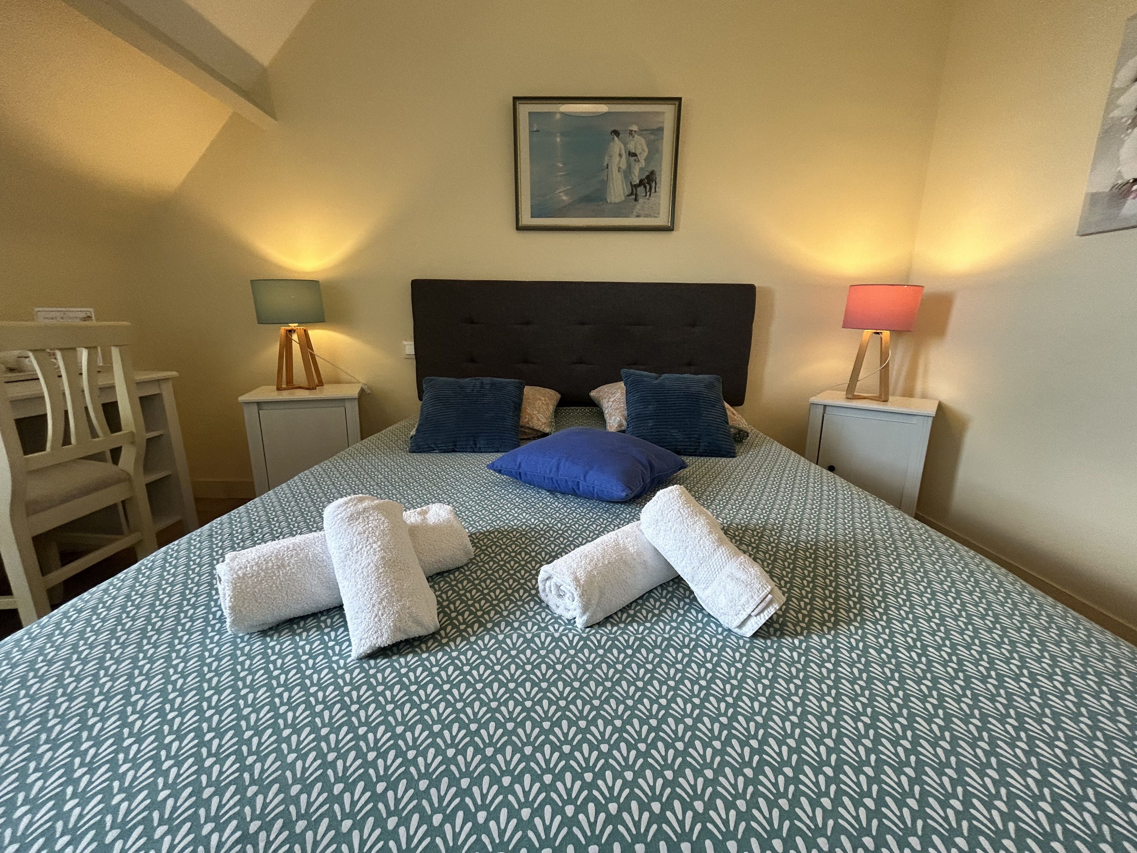 Una cama bien hecha con un edredón estampado, dos almohadas y toallas enrolladas.