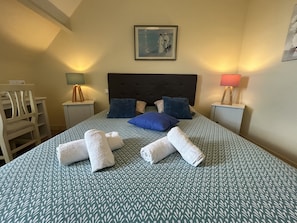 Una cama bien hecha con un edredón estampado, dos almohadas y toallas enrolladas.
